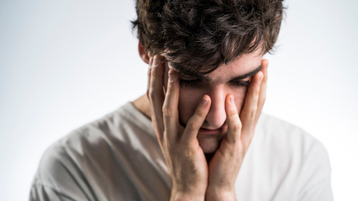 Sad man holding face with white shirt and black hair